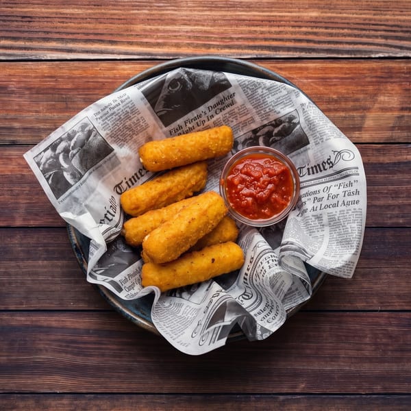Golden fried mozzarella sticks and a small bowl of marinara sauce on newspaper in a basket.