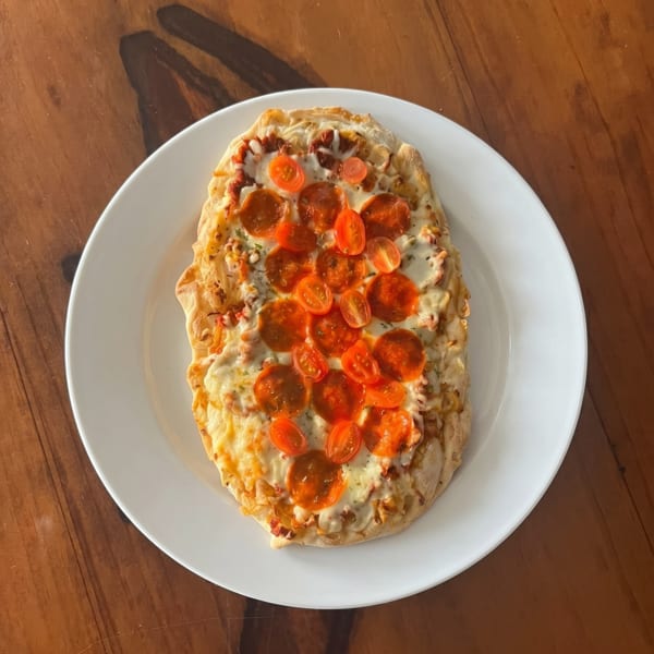 A rectangular flatbread pizza with melted cheese, pepperoni, and halved cherry tomatoes on a white plate.