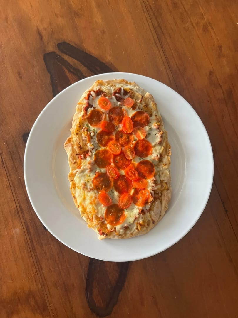 A rectangular flatbread pizza with melted cheese, pepperoni, and halved cherry tomatoes on a white plate.