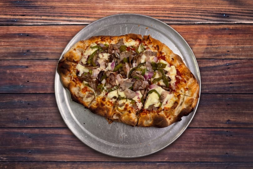 A freshly baked pizza with green peppers, red onions, and meat on a metal pan.